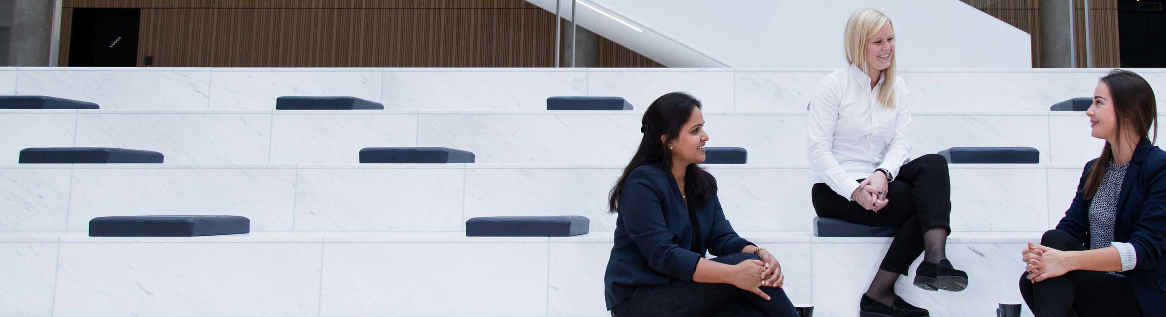 Three young female DSV trainees sitting on the stairs at the DSV headquarter in Hedehusene